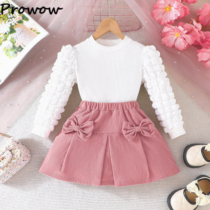 White long-sleeve top and pink skirt with a bow on a hanger against a floral background.

