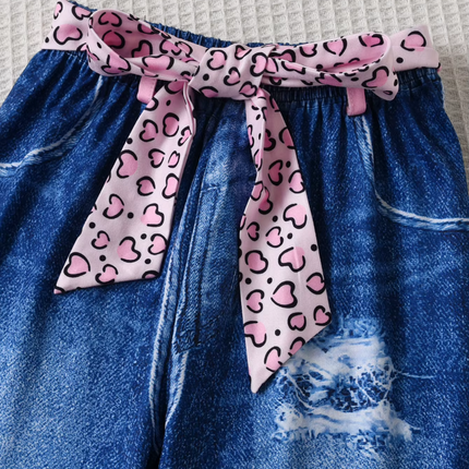 Blue denim shorts with a pink leopard print ribbon tied around the waist on a light background.

